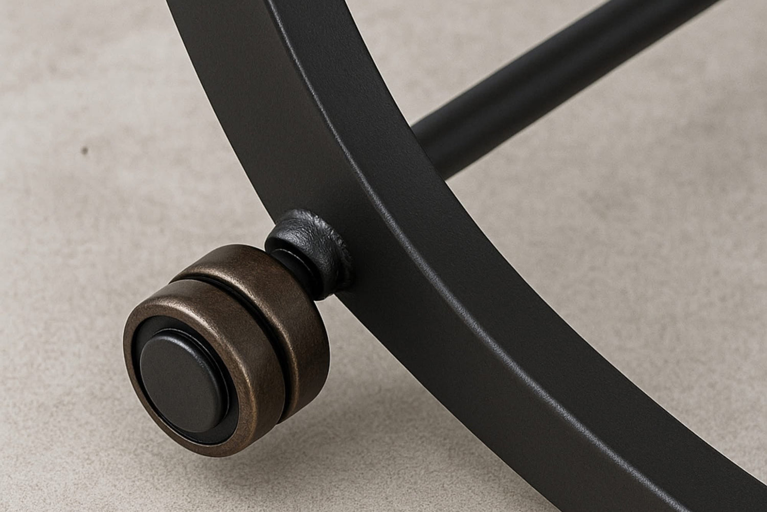 Close-up of a black metal chair leg with a bronze caster wheel on a beige background